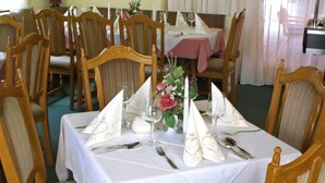 A dining table set for four with white tablecloths, wooden chairs, and a centerpiece of flowers and candles. - Hotel garni Schmideler (Sonthofen)