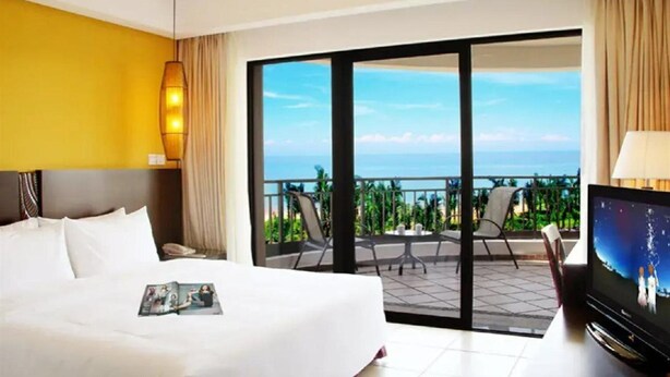Habitació d'hotel amb llit, televisió i un balcó amb vista a l'oceà.