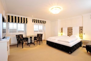 A hotel room with a large bed, two armchairs, a desk, and a small table.
