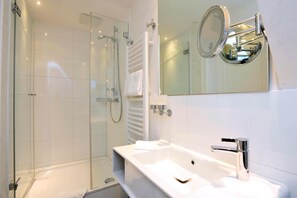 A modern bathroom with a glass-enclosed shower, a white sink with a chrome faucet, and a mirror with a chrome frame. - Strandhoern (Wenningstedt-Braderup)