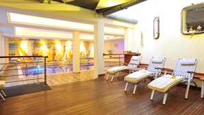 A sunlit room with wooden flooring, a pool area with colorful murals, and several sun loungers.