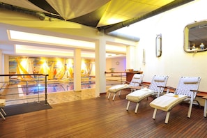 A sunlit room with wooden flooring, a pool area with colorful murals, and several sun loungers.