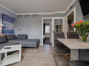 A modern living room with a grey sofa, a white side table, and a dining area with a table and chairs.