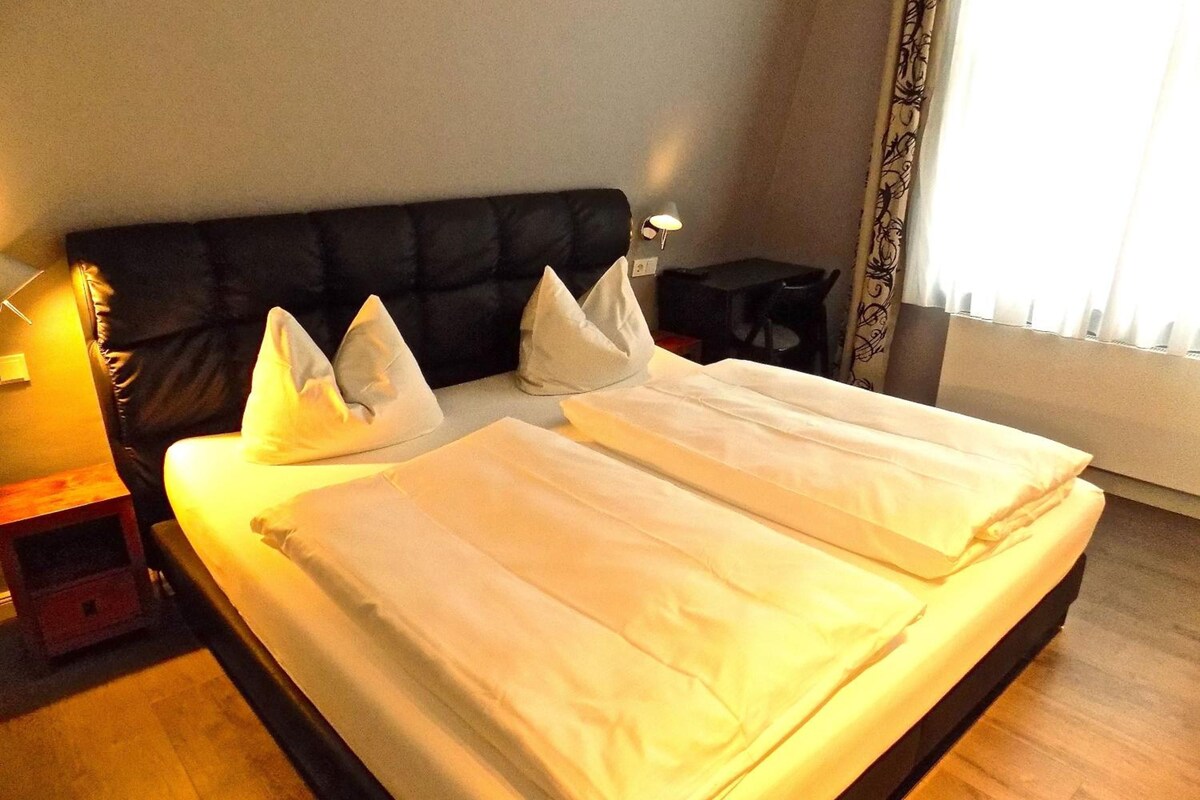 Ein Hotelzimmer mit einem Bett, Kissen, einem Nachttisch und einer Lampe.