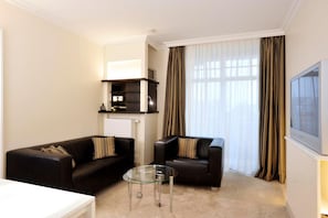 A modern living room with two black sofas, a glass coffee table, and a television on the wall.