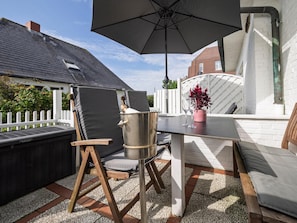 An outdoor patio with a table, chairs, a large umbrella, and a potted plant.