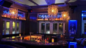 A bar area with a curved counter, multiple hanging chandeliers, and a view of the outside through large windows.
