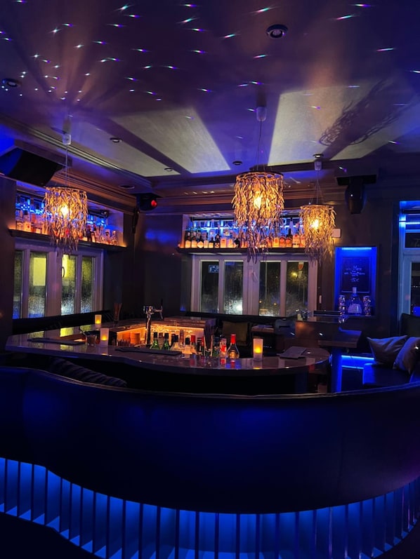 A bar area with a curved counter, multiple hanging chandeliers, and a view of the outside through large windows.