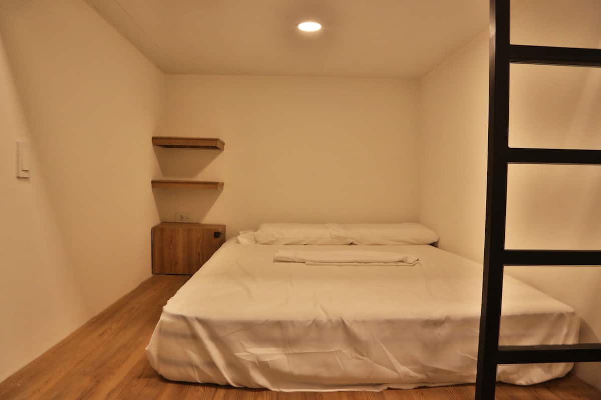 A small, single-bed room with a wooden floor, a white bedspread, and a wooden nightstand.
