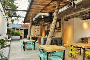An indoor dining area with wooden tables and chairs, a brick wall, and a ceiling with exposed beams and lighting fixtures. - Santuario Getsemaní Hostel (Cartagena)