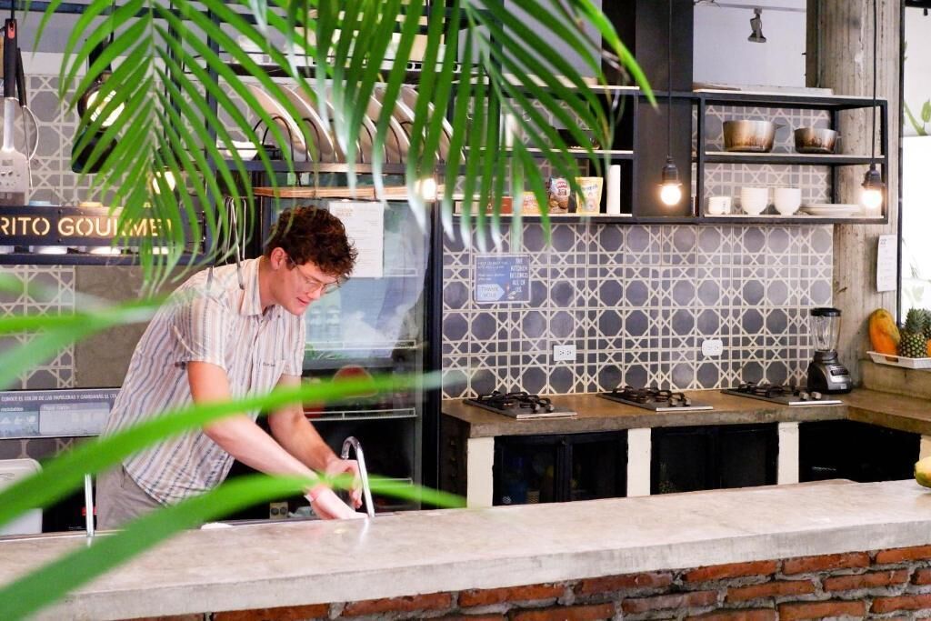 A kitchen area with a countertop, a stove, and a shelf with kitchenware.