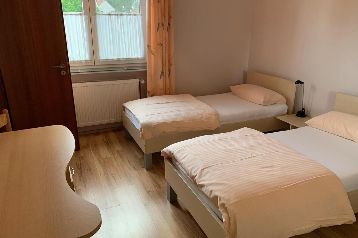 A room with two single beds, a wooden table, and a radiator.