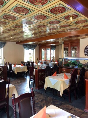 A restaurant interior with ornate ceiling tiles, wooden furniture, and a fish tank.