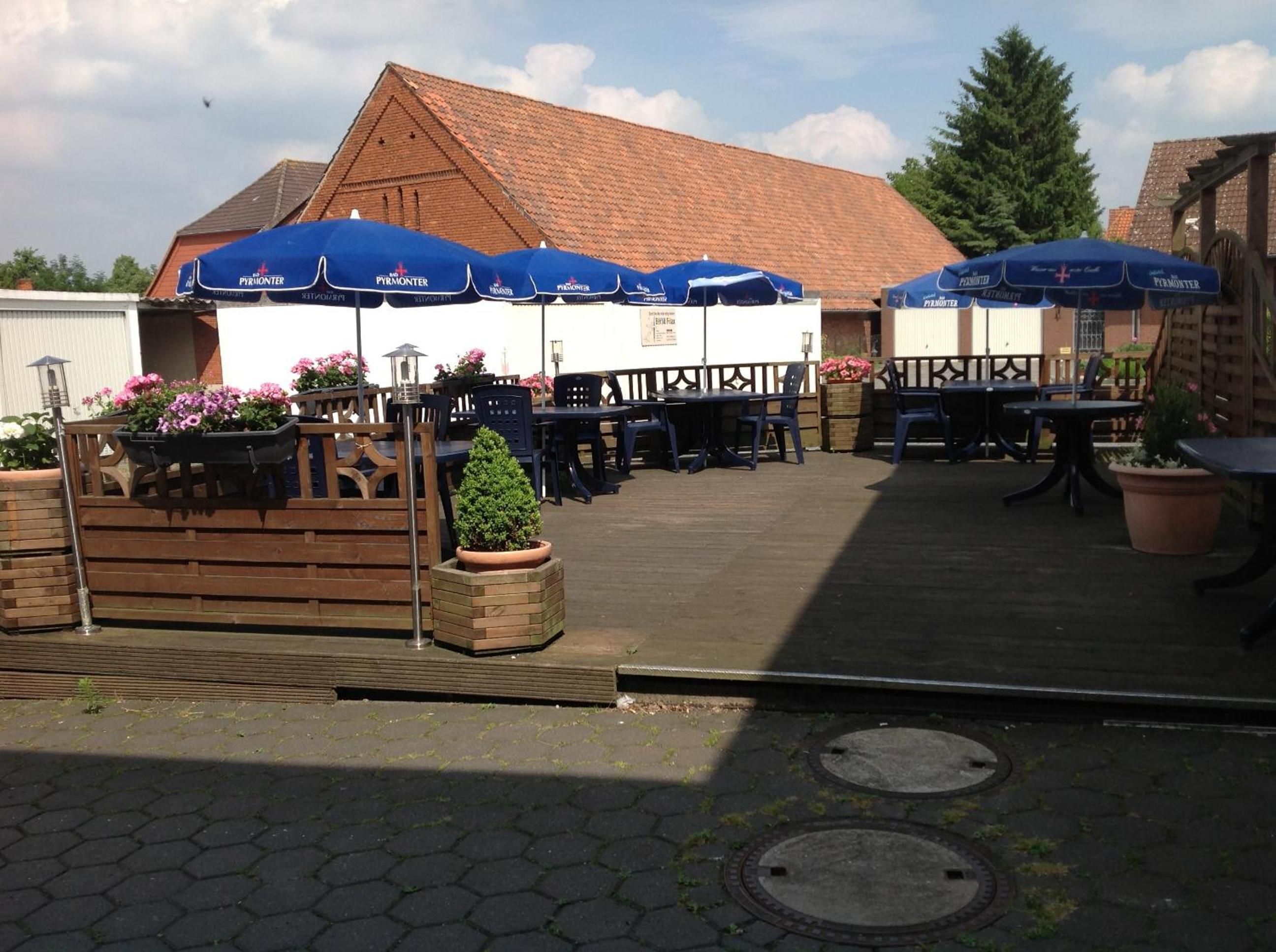 Ein Sitzbereich im Freien mit Tischen und Stühlen, blauen Sonnenschirmen und Topfpflanzen.