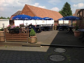 An outdoor seating area with tables and chairs, blue umbrellas, and potted plants.