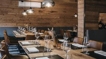 Un ristorante con pareti in legno, diversi tavoli apparecchiati con bicchieri da vino e posate, e lampade a sospensione.
