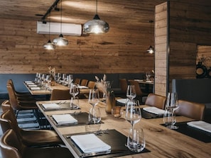 A restaurant with wooden walls, multiple tables set with wine glasses and cutlery, and pendant lighting.