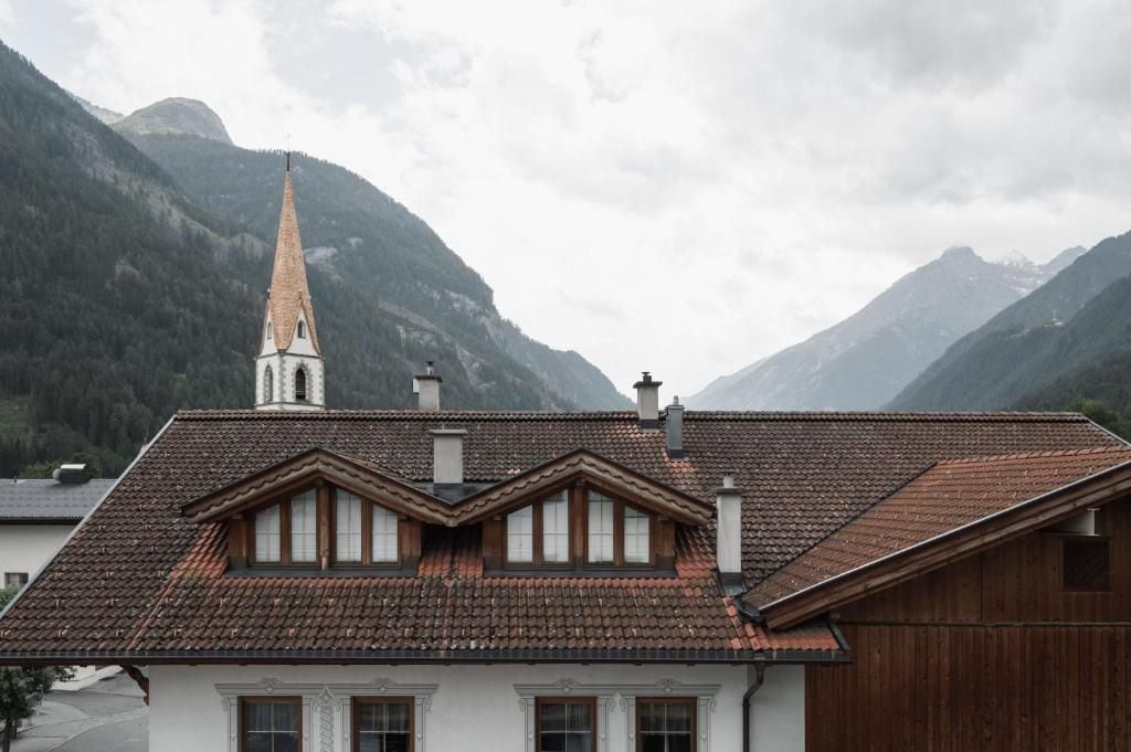 Un edificio con un tetto ripido, una torre imponente e montagne sullo sfondo.