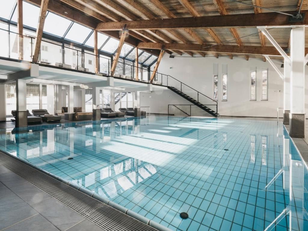 Una piscina interior con suelo de cristal, vigas de madera y una escalera que lleva a un nivel superior.