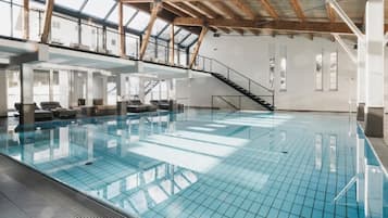 Una piscina interna con pavimento in vetro, travi in legno e una scala che conduce a un livello superiore.