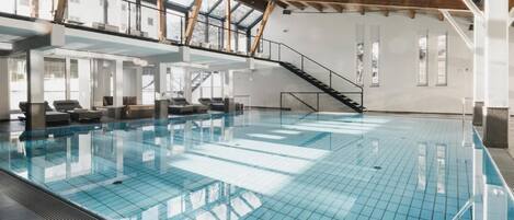 Una piscina interior con suelo de cristal, vigas de madera y una escalera que lleva a un nivel superior.