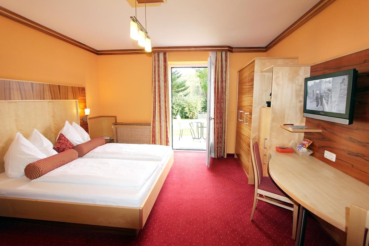 A hotel room with a bed, a desk, a television, and a view of the outdoors.