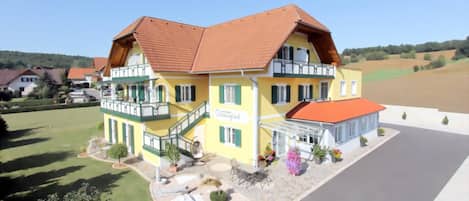 A two-story building with a balcony, a covered porch, and a landscaped front yard.