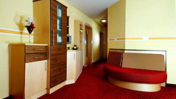 Ein kleines Hotelzimmer mit Küchenzeile, einem roten Schlafsofa und einem Holzschrank.