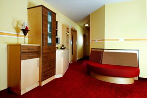 A compact hotel room with a kitchenette, a red sofa, and a wooden cabinet. - Hotel Garni Thermenglv Ck (Unterlamm)