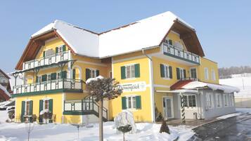 Un edificio de varios pisos con techo cubierto de nieve y contraventanas verdes, con un letrero que dice 'Herzlich Willkommen' (Bienvenido).