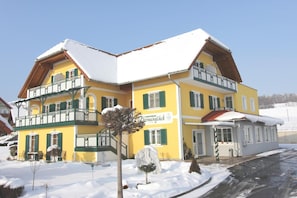 A multi-story building with a snow-covered roof and green shutters, featuring a sign that reads 'Herzlich Willkommen' (Welcome). - Hotel Garni Thermenglv Ck (Unterlamm)