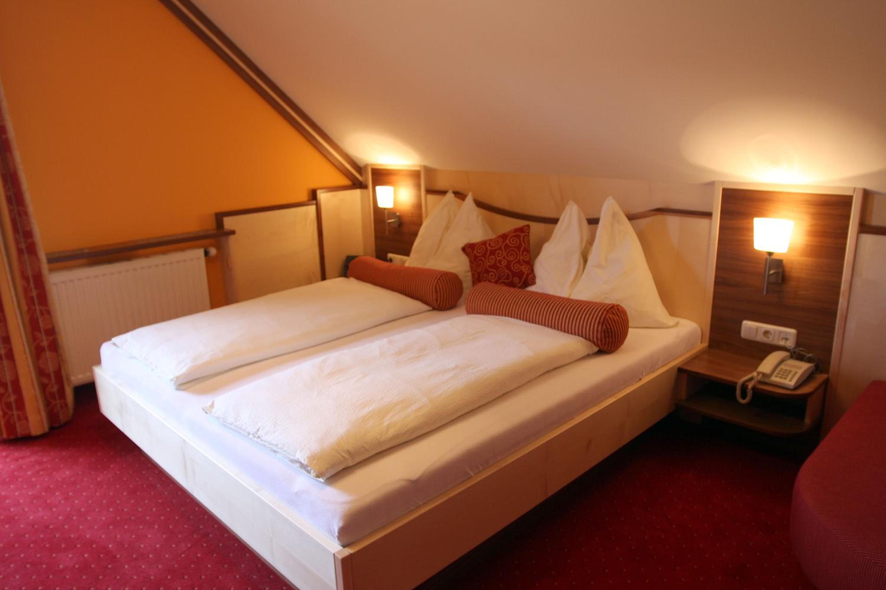 A hotel room with a double bed, two bedside tables with lamps, a red carpet, and a telephone on the right side.