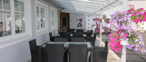 An outdoor patio with wicker furniture, stone flooring, and hanging flower baskets.