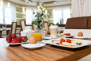 A breakfast setting with plates of food, a vase of flowers, and a coffee mug. - Hotel Garni Thermenglv Ck (Unterlamm)