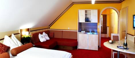 A hotel room with a bed, a sofa, a kitchenette, and a dining area.