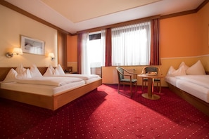 Una habitación de hotel con cama, escritorio, silla y ventana con cortinas.