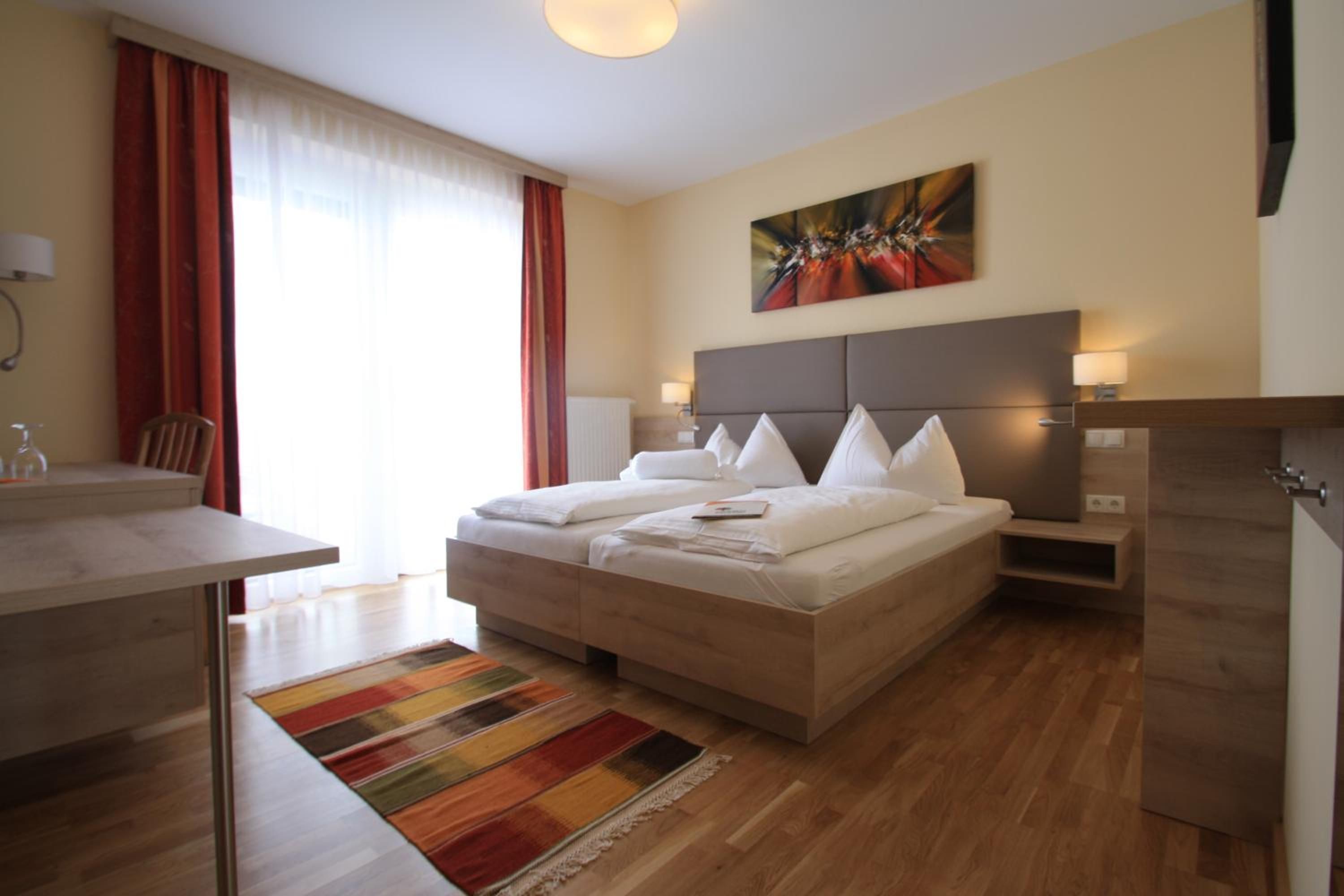 A modern hotel room with a large bed, bedside tables, a desk, and a colorful rug.