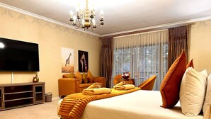 Habitación de hotel con una cama grande, un televisor de pantalla plana, un sofá y una mesa de comedor con vistas al exterior.