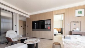 Une chambre d’hôtel moderne dotée d’un coin salon, d’une télévision à écran plat, d’un minibar et d’un grand miroir.