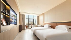 Une chambre d’hôtel avec un grand lit, un téléviseur fixé au mur et une vue sur la ville par la fenêtre.