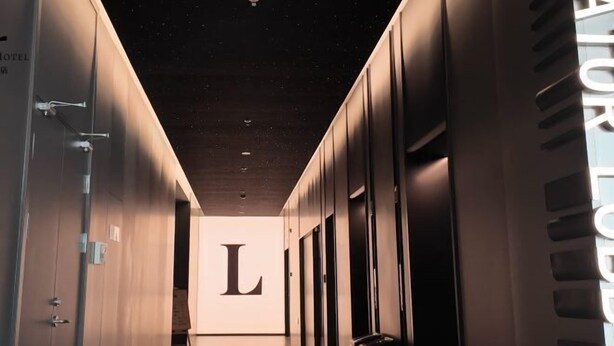 Un couloir d’hôtel avec un grand « L » peint sur le mur, indiquant un numéro de chambre ou une zone spécifique.