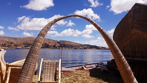 Una estructura tradicional con techo curvo, una silla de madera y vista a un lago con barcos.