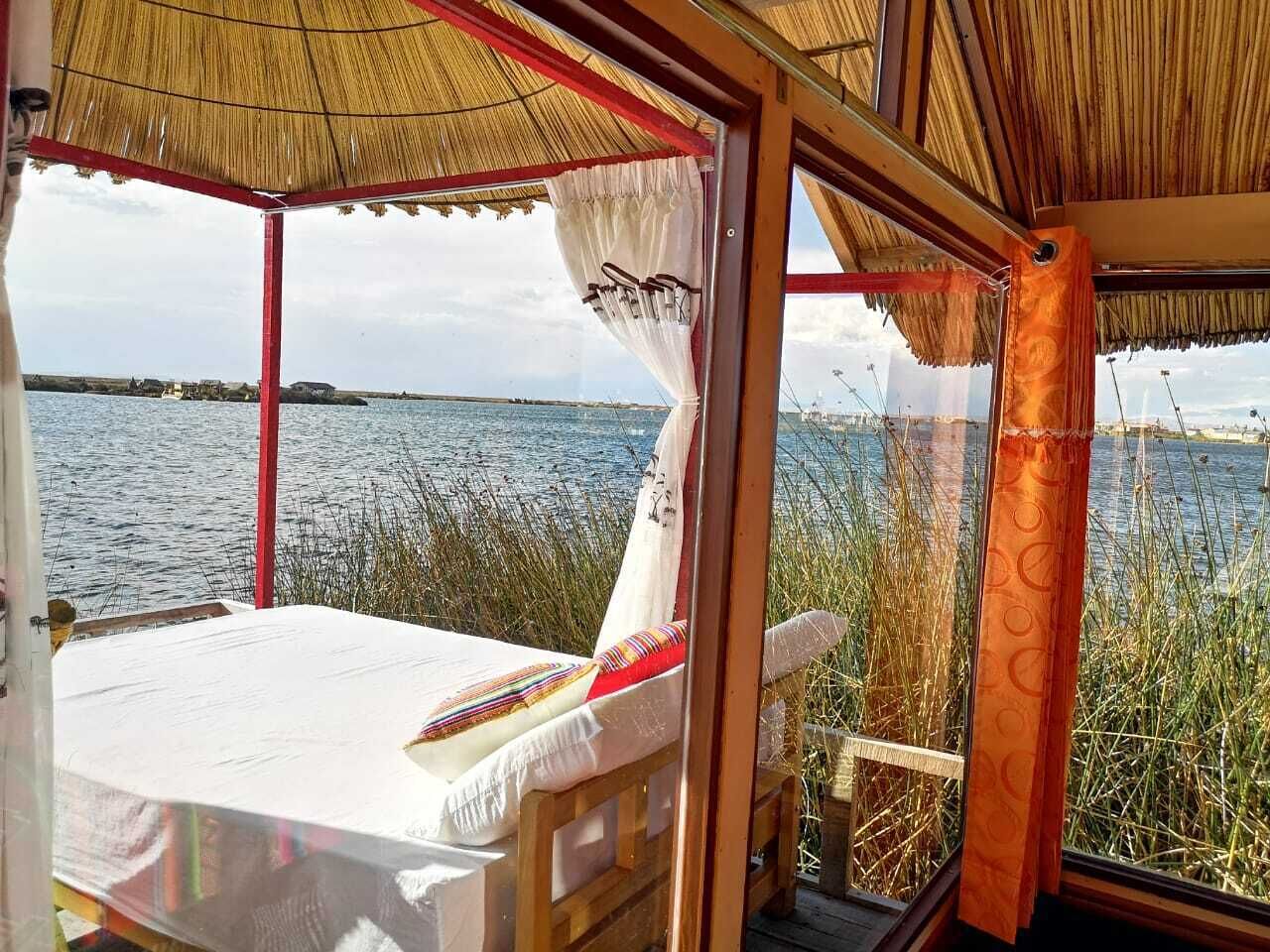 A room with a view of a body of water, a bed, and a window with a curtain.