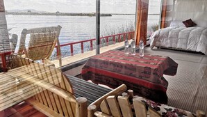 Una habitación acogedora con una cama, una silla de madera, una mesa con mantel rojo y vista al agua.