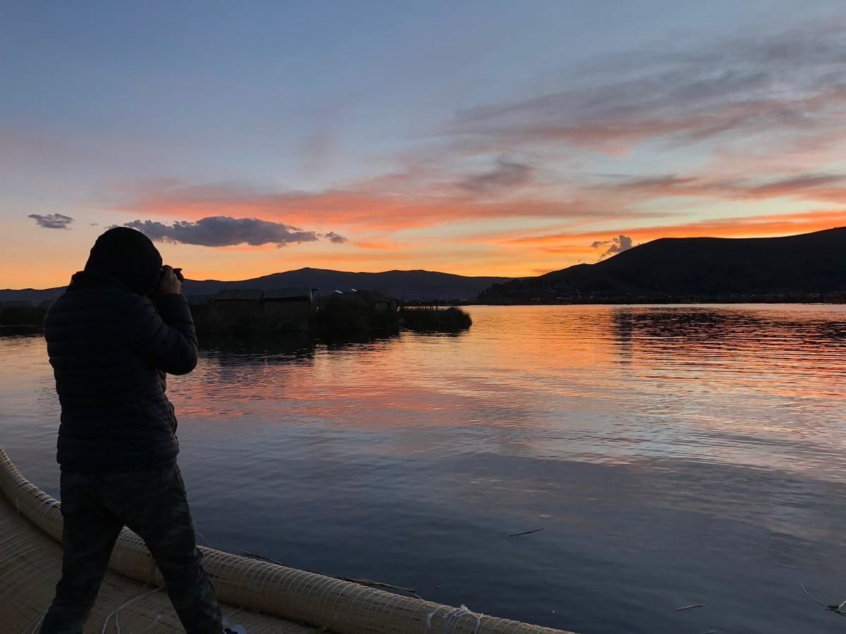 A person standing on a dock at sunset, overlooking a calm body of water with distant hills.