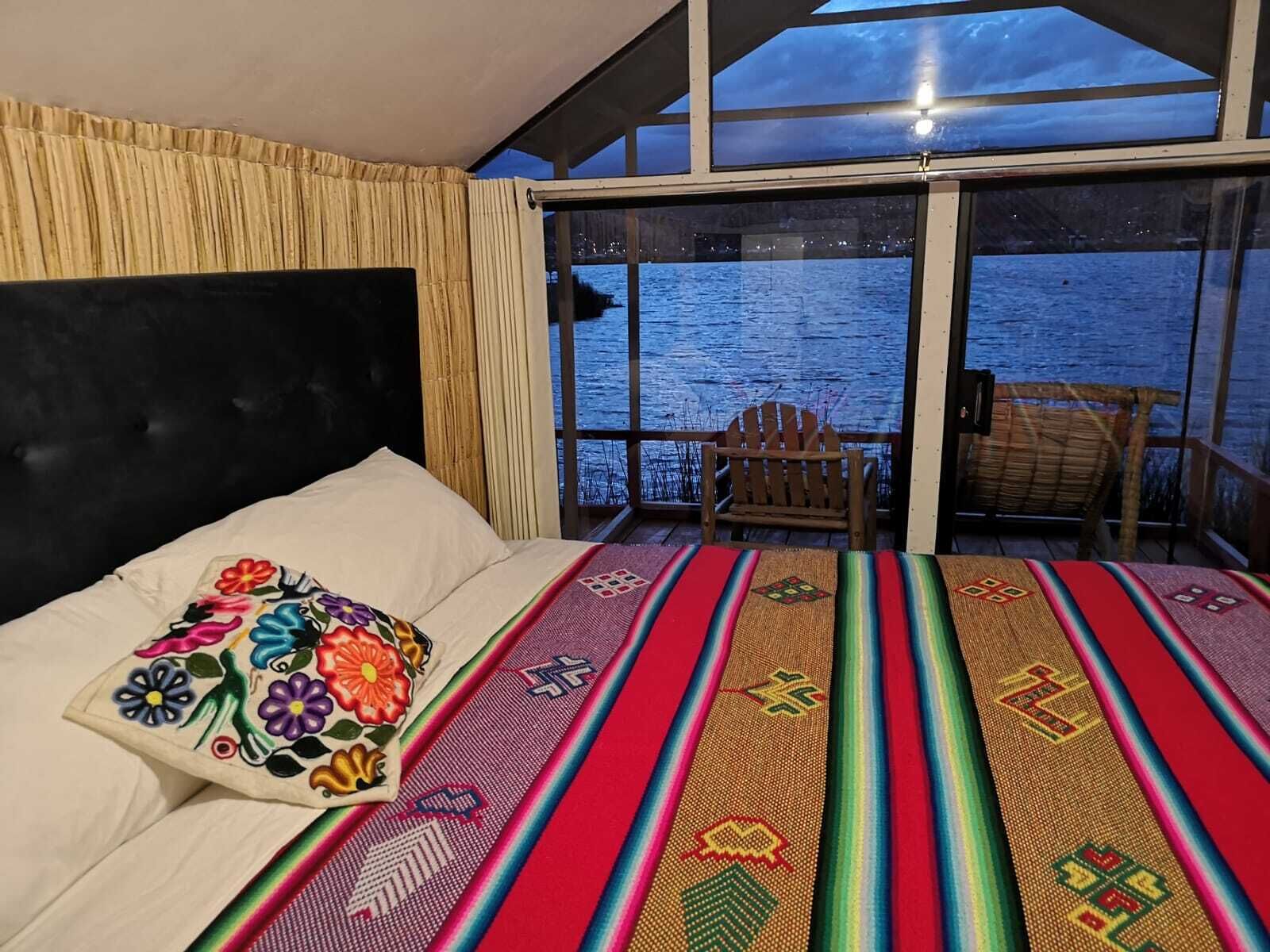 A bedroom with a bed, a chair, and a view of the water through large windows.