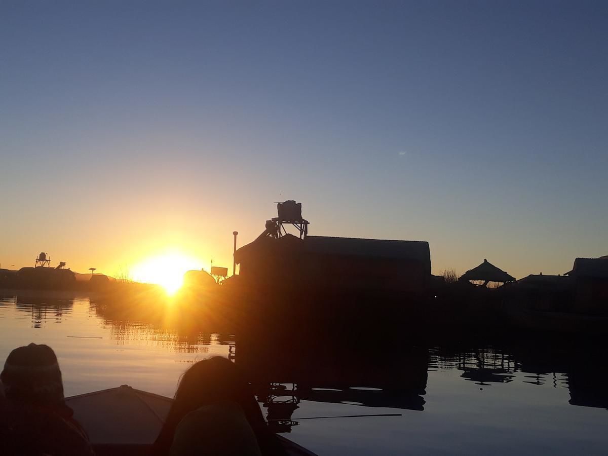 A sunset over a body of water with a building silhouette and a chair on a dock.