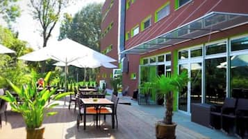 An outdoor patio area with tables and chairs, surrounded by glass doors and windows.