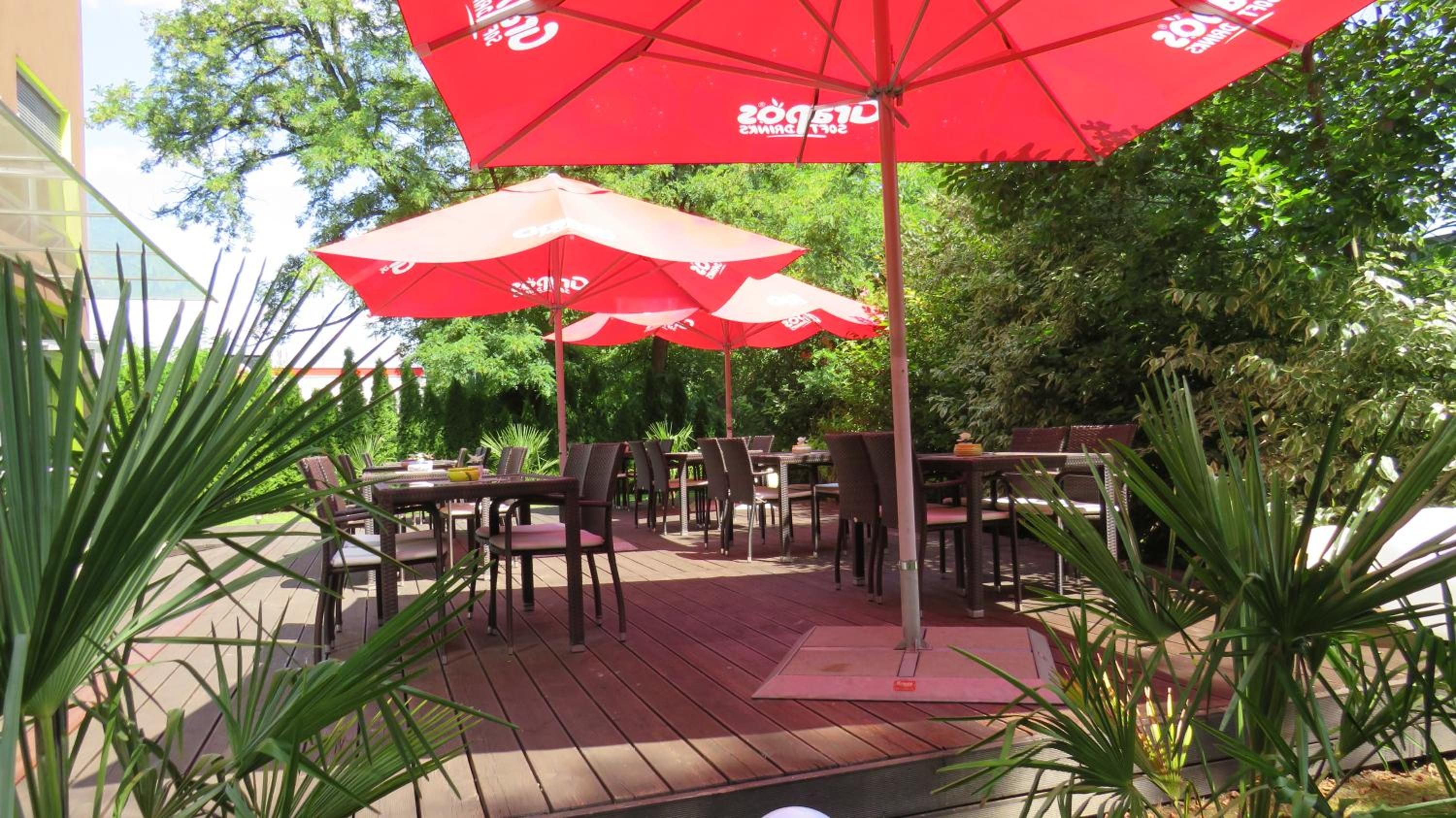 An outdoor dining area with red umbrellas, wooden tables, and chairs.