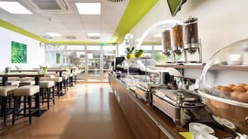 Buffet-alue, jossa on tarjoilutiski, ruoka-annostelulaitteet ja istumapaikkoja.